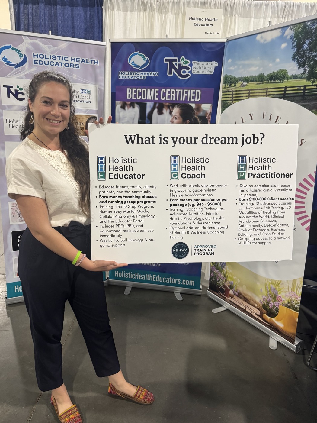 Amy Sprouse at a Holistic Health Educators expo booth holding the What Is Your Dream Job board